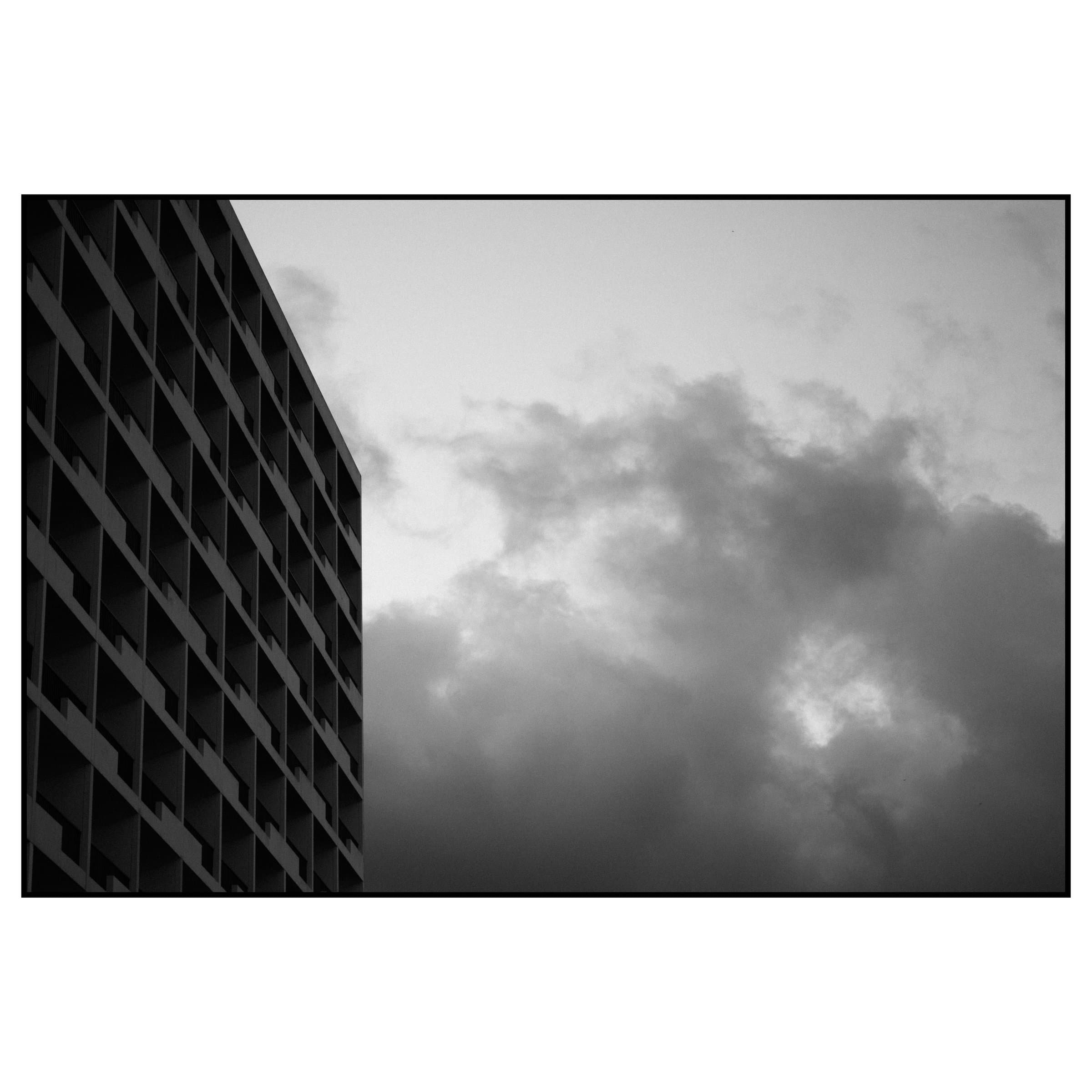 Brütalist beton binanın geometrik cephesi ve arkadaki fırtına bulutları