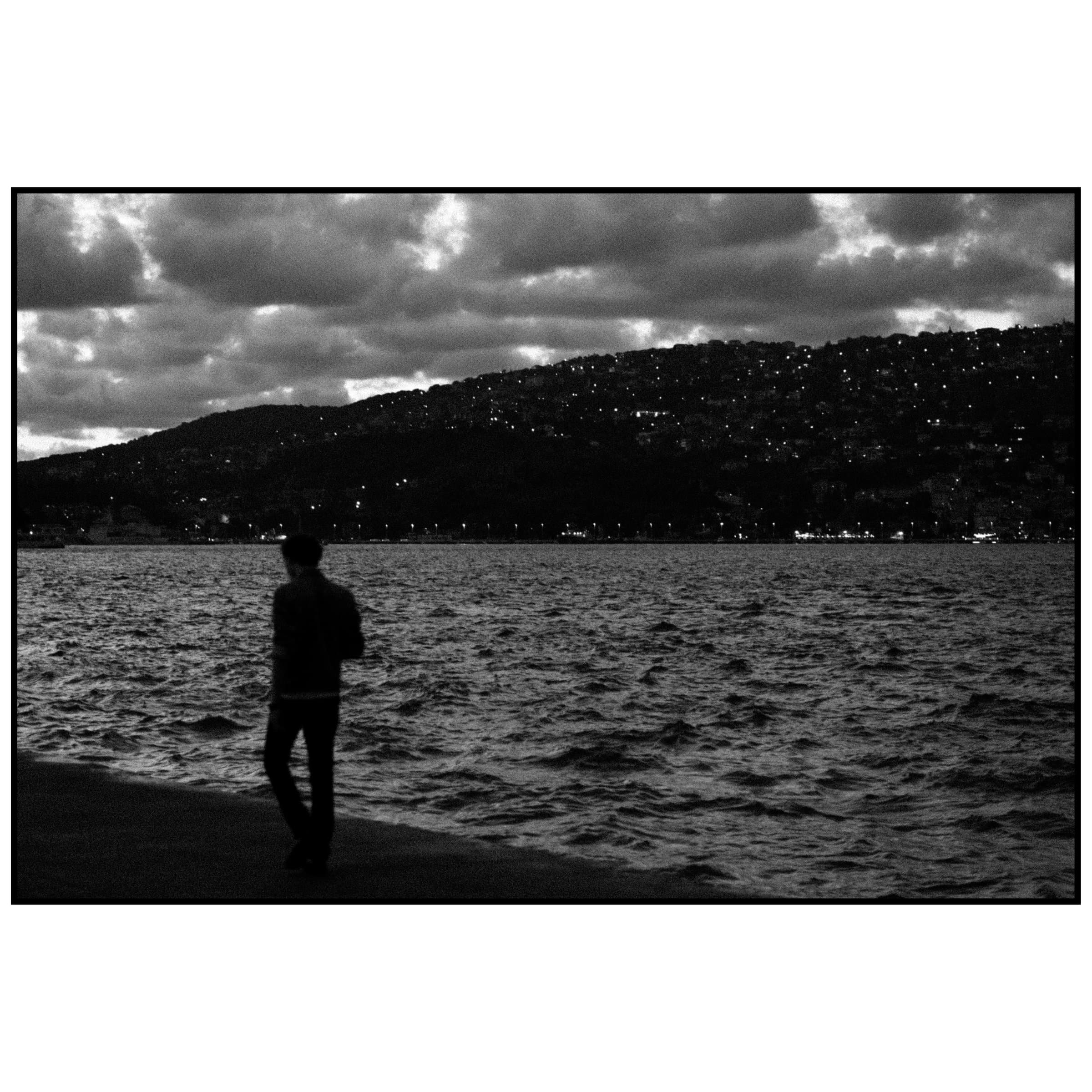 Boğaz kıyısında yürüyen sırt çantalı adamın silueti ve arkadaki tepe